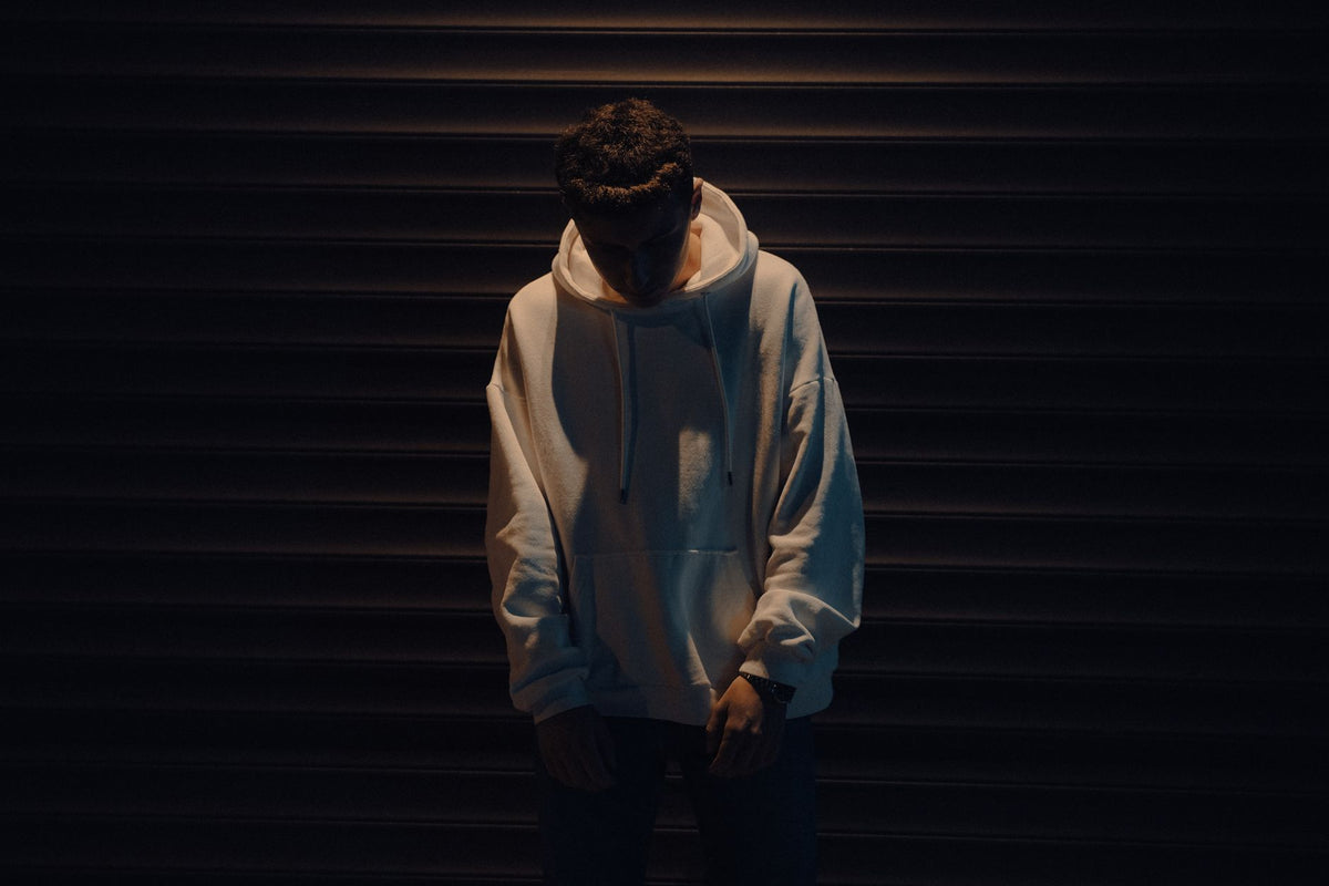 Homme en sweat à capuche oversize crème devant un rideau métallique sombre, base du look grunge homme