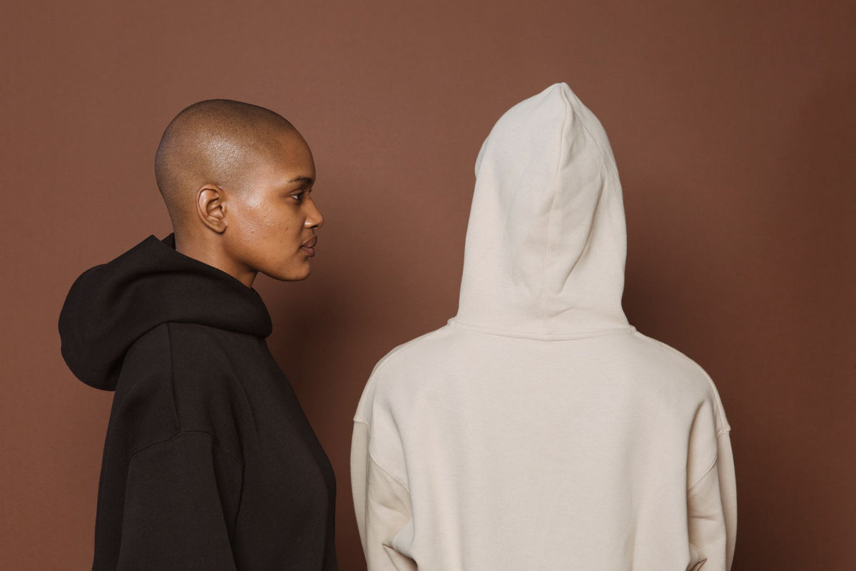 Sweat oversize femme porté en noir et en écru, capuche relevée, sur fond studio brun