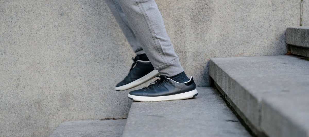 Bas de jogging gris qui tombe sur des sneakers noires en descendant un escalier extérieur