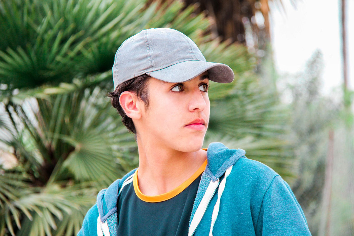 Comment nettoyer une casquette : jeune homme portant une casquette grise unie dans un look streetwear décontracté