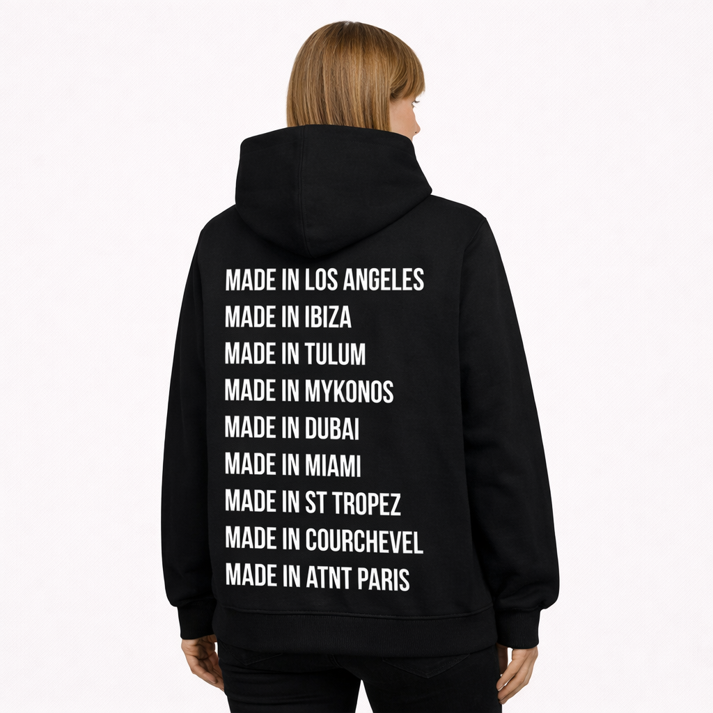 Mannequin femme portant un sweat à capuche noir ATNT Paris, vue de dos en angle trois-quarts, message typographique « Made in » listant des destinations internationales, style streetwear