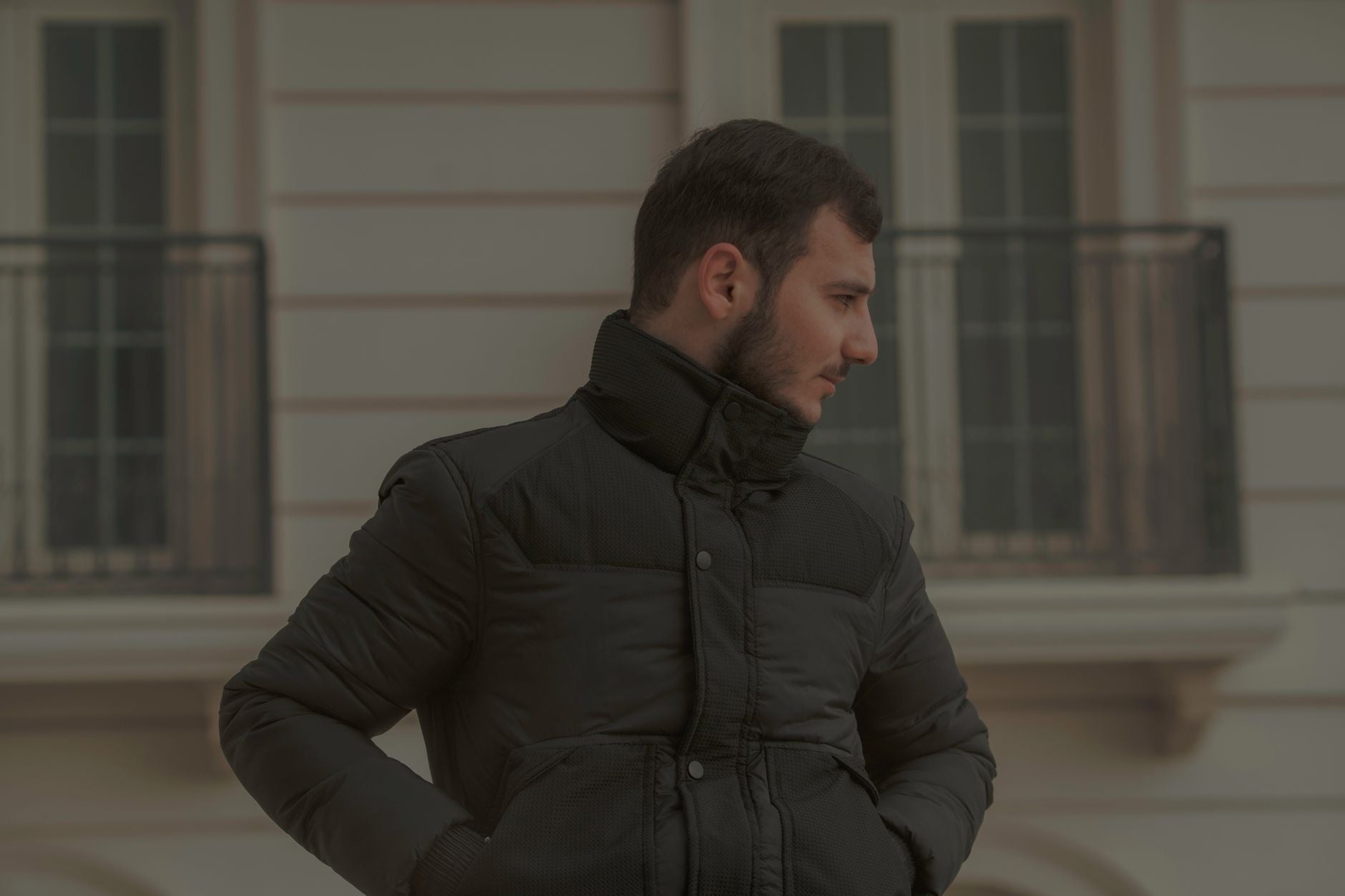 Homme en blouson matelassé noir posant devant une façade urbaine élégante