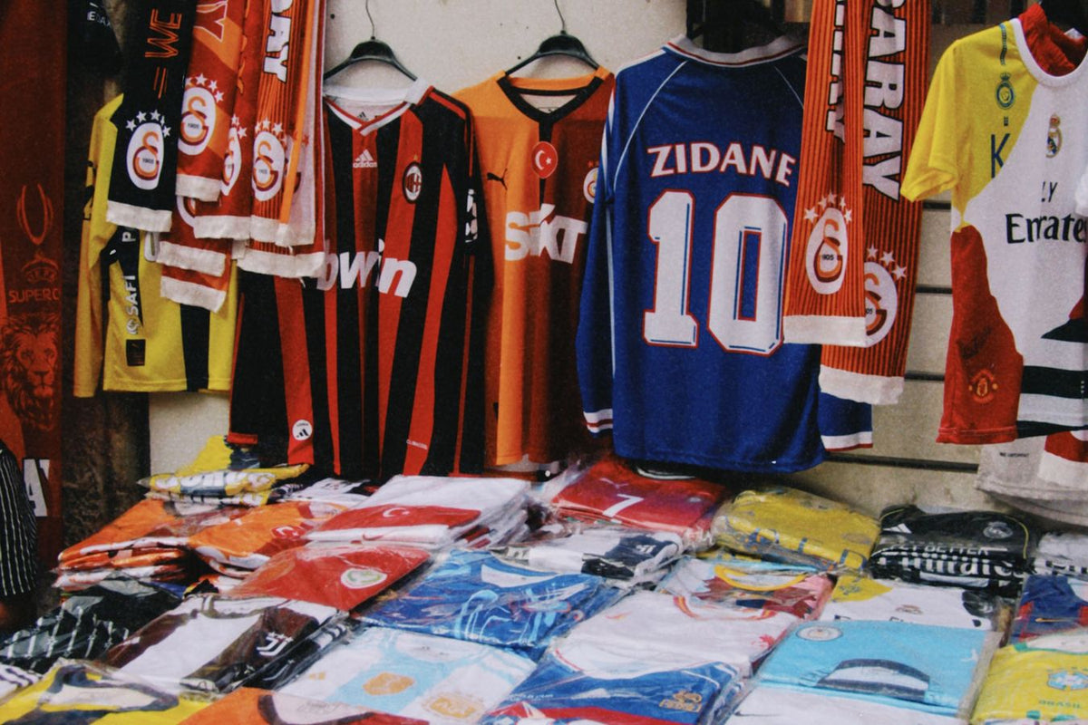Mur de maillots de foot collector suspendus sur un étal, dont un maillot France floqué Zidane