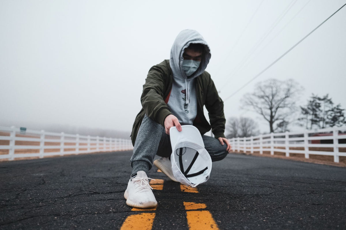 Casquette tendance homme : jeune homme en hoodie tenant une casquette blanche sur une route brumeuse, style urbain streetwear